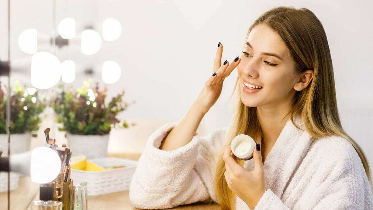 Cum să ai grijă de tenul tău în 7 pași simpli young beautiful blonde girl cares face skin with moisturizer front mirror