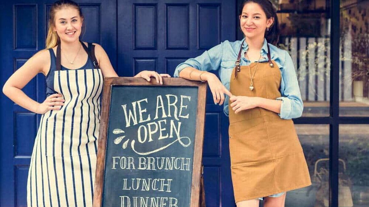 Cheerful,Business,Owners,Standing,With,Open,Blackboard