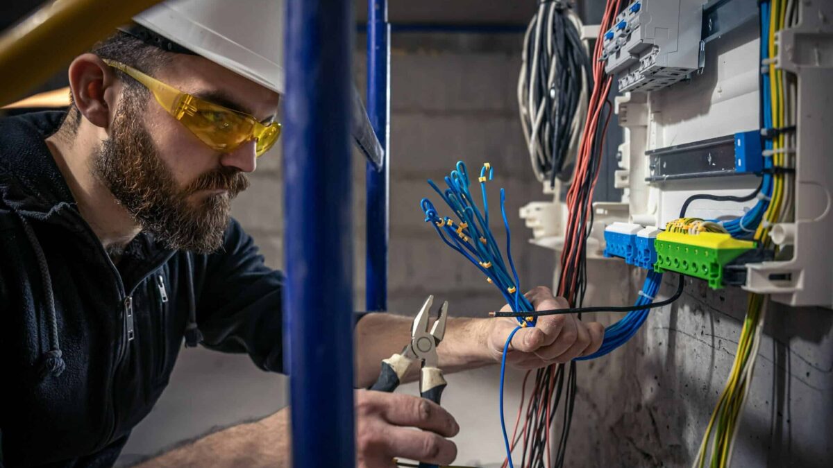 A male electrician works in a switchboard with an electrical connecting cable.