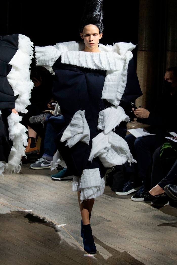 Un model feminin de podium într-o rochie sculpturală, cu umeri largi, în negru, cu volane ample albe