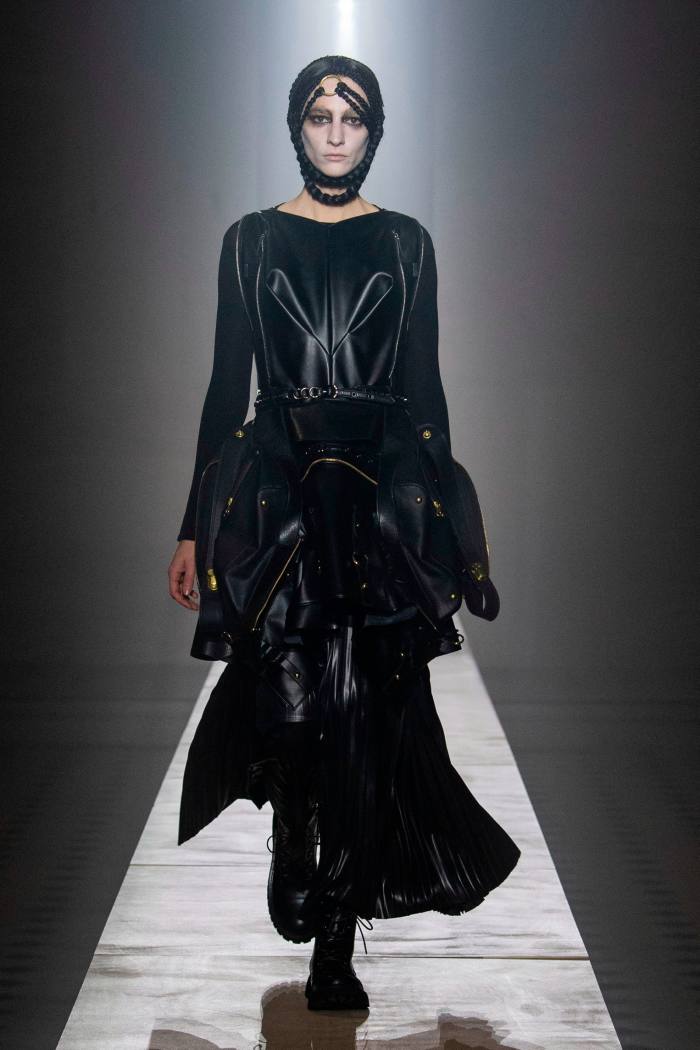 Un model feminin de podium, într-o rochie neagră severă, mătăsoasă și accesoriu negru