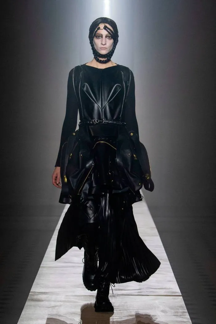 Un model feminin de podium, într-o rochie neagră severă, mătăsoasă și accesoriu negru