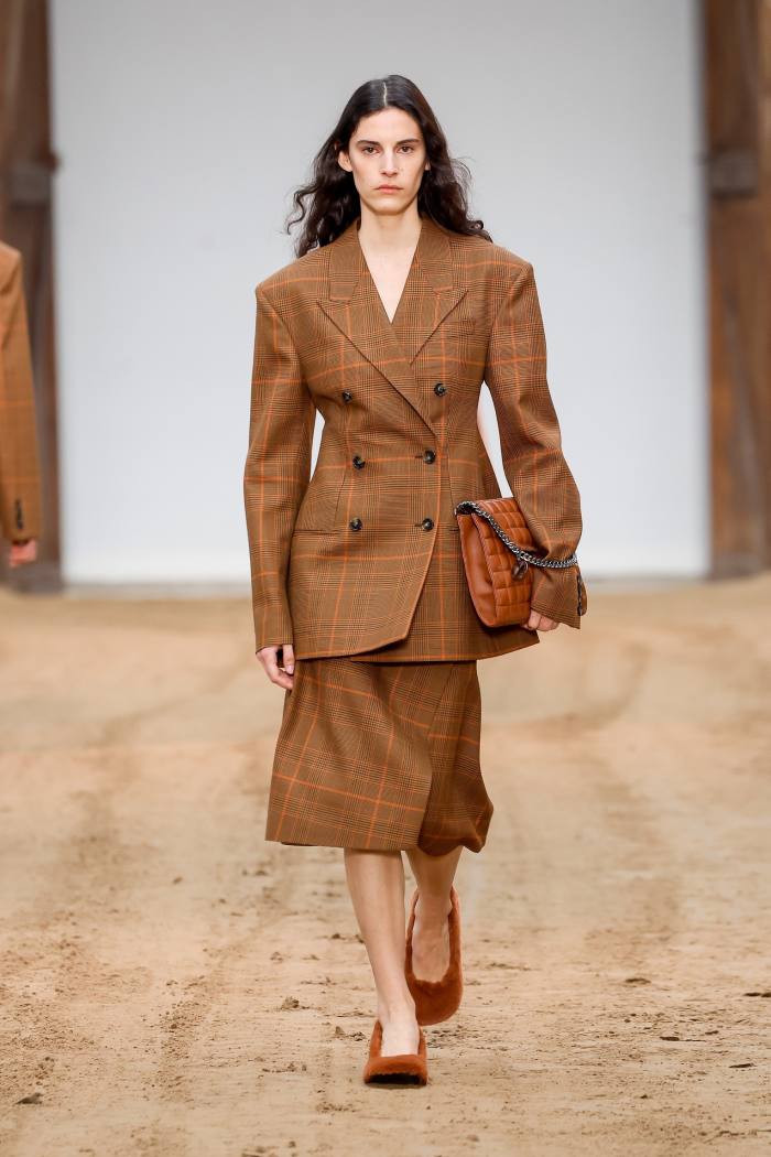 Un model feminin de podium într-un blazer clasic maro cu carouri și o fustă asortată