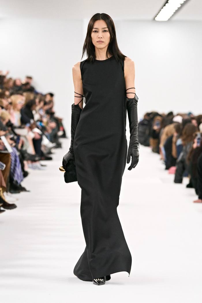 Un model feminin de podium într-o rochie de seară neagră, lungă și elegantă, fără mâneci, dar cu mănuși negre până la cot