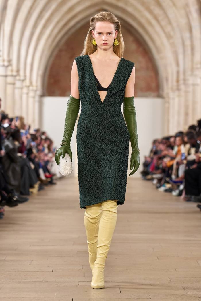 Un model feminin de podium într-o rochie fără mâneci verde închis și cizme galbene înalte