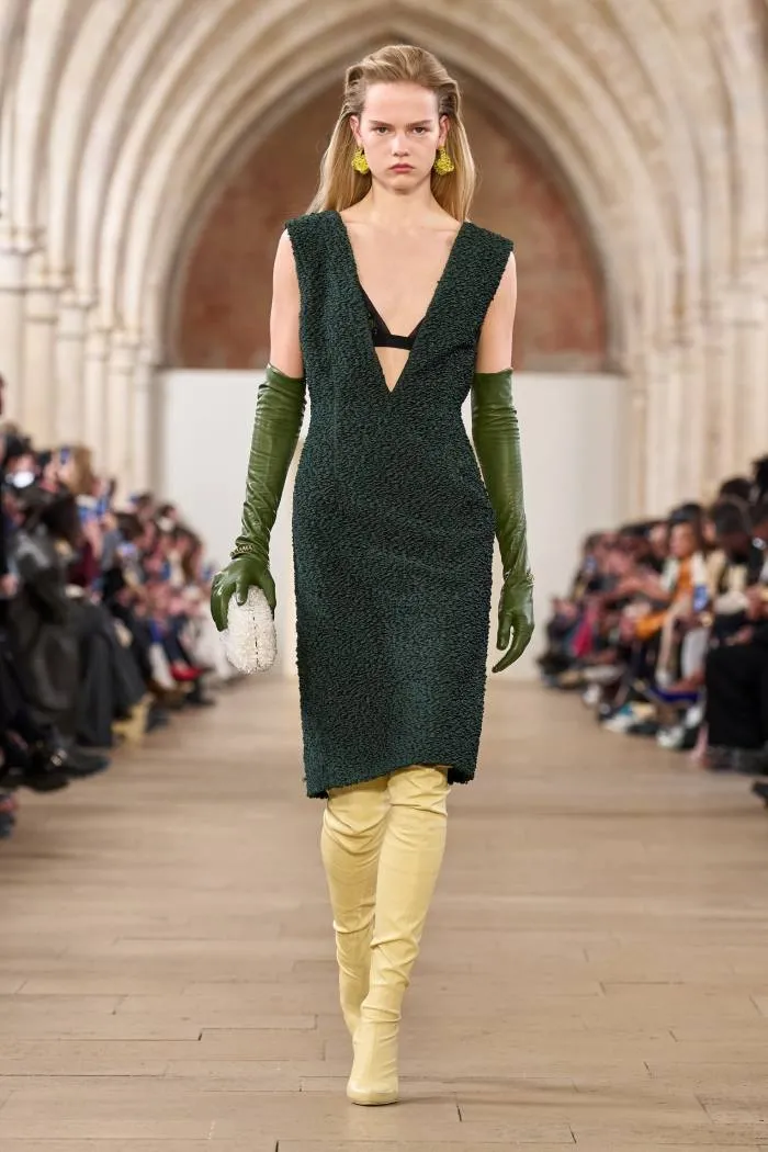 Un model feminin de podium într-o rochie fără mâneci verde închis și cizme galbene înalte