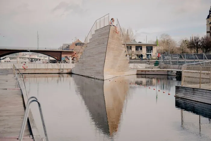 Scăldatori așezați deasupra unui turn triunghiular de sărituri din lemn la Baia portului Islands Brygge