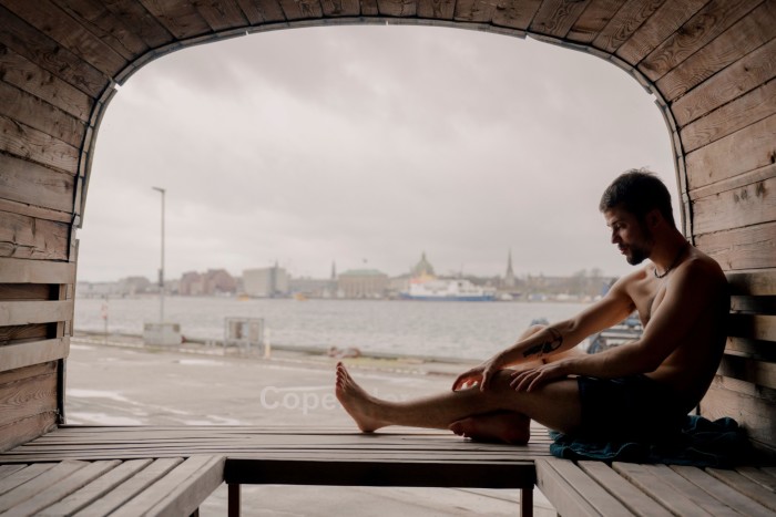 Un bărbat topless așezat lângă fereastră la capătul îndepărtat al Saunei panoramice CopenHot 