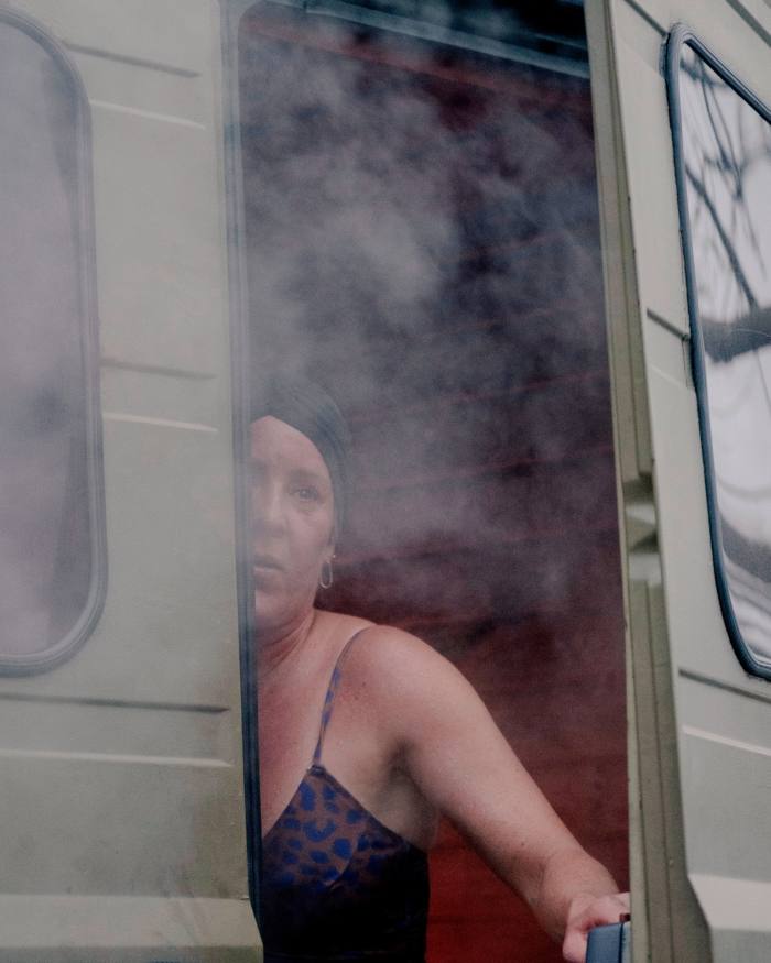 O femeie în costum de baie, privind pe ușa din spate de la duba saună Butcher's Heat