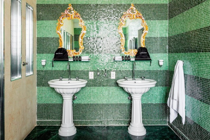 Două chiuvete albe și două oglinzi cu rame aurite într-o baie cu gresie verde