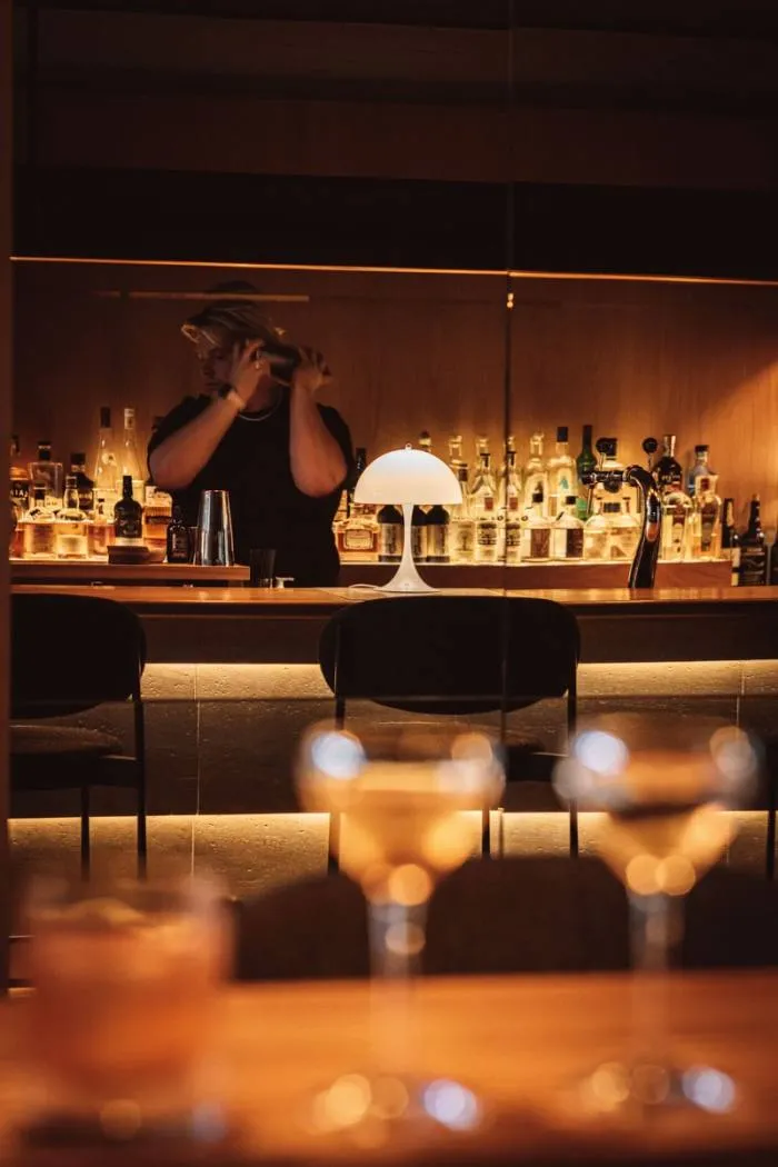 Restaurantul Héroine slab luminat, cu un barman care ține un shaker de cocktail 