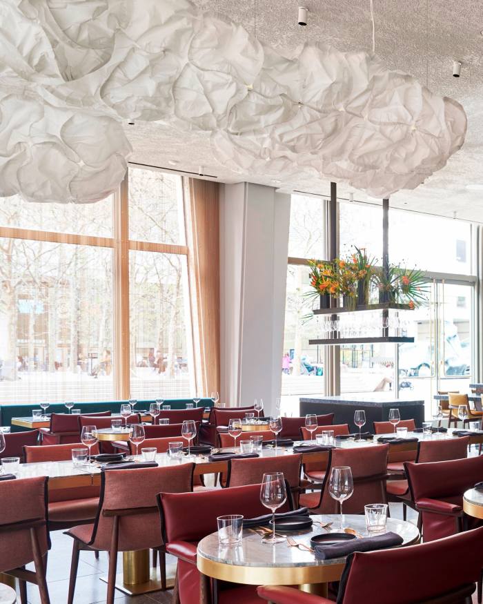Ghidul gastronomic al lui Dawn Davis la New York Scaune roșii la mesele cu blat de marmură cu ramă aurie, sub o sculptură de iluminat mare, în formă de nor, atârnată de tavan, la Tatiana lui Kwame Onwuachi la Lincoln Center