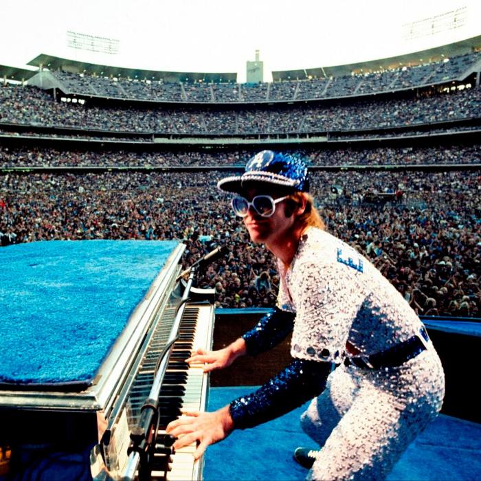 Elton John cântă la pian pe scenă într-o arenă plină