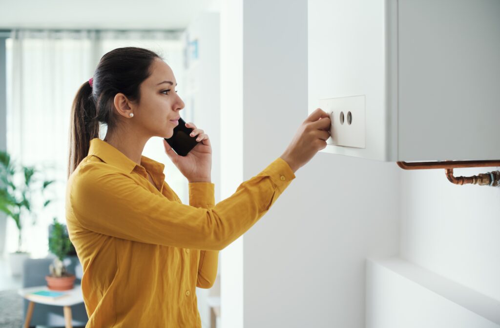 Cum afectează creșterea costului vieții îmbunătățirile locuințelor în 2023 Poza cu o femeie îngrijorată la telefon cu o mână pe boiler