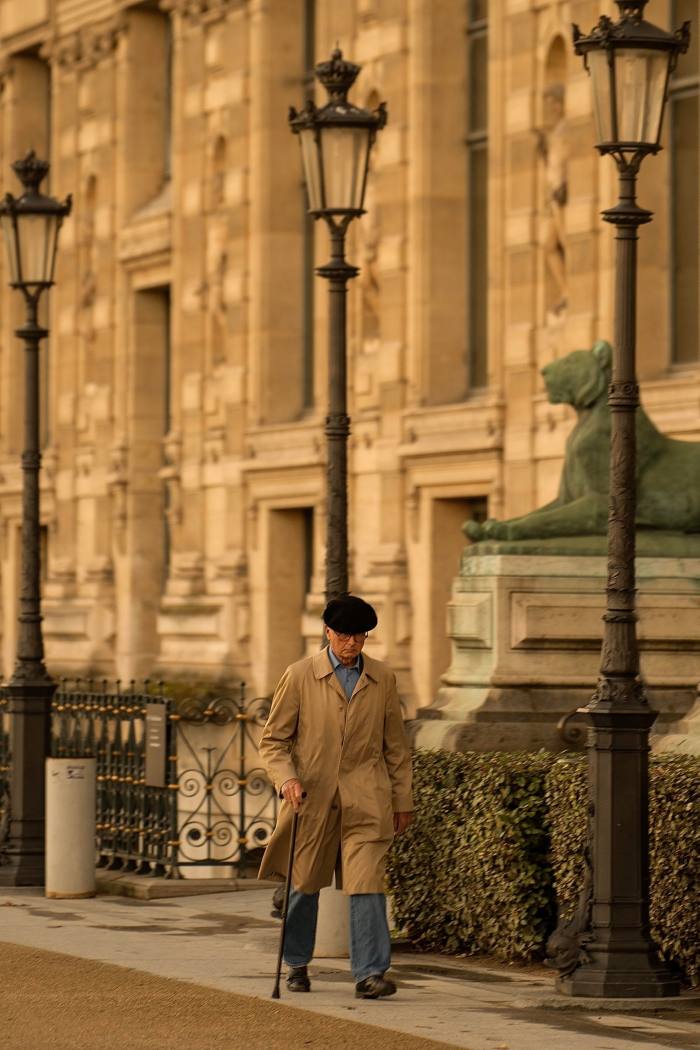 Un bărbat care merge pe stradă într-o haină maro și un baston