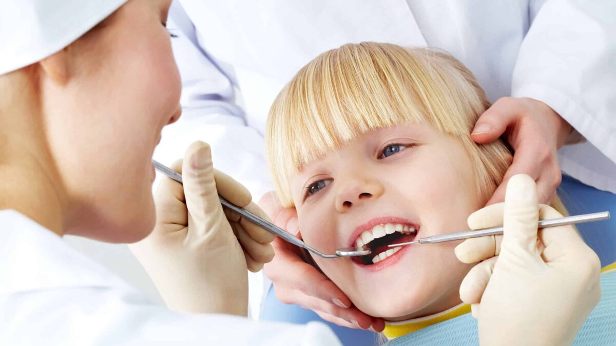Image of little girl having teeth checked by doctor and assistant