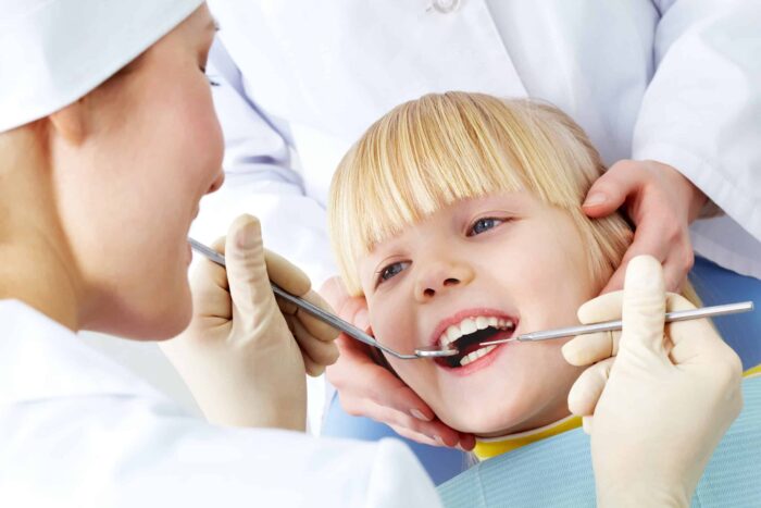 Image of little girl having teeth checked by doctor and assistant