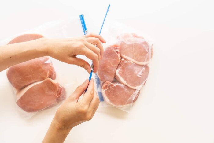 Raw boneless pork loin chops in zipper storage bags. Woman packs meat in bags
