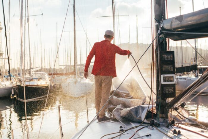 sailboat owner yachtsman uses hose wash salt water from yachr deck when docked parked marina sunset