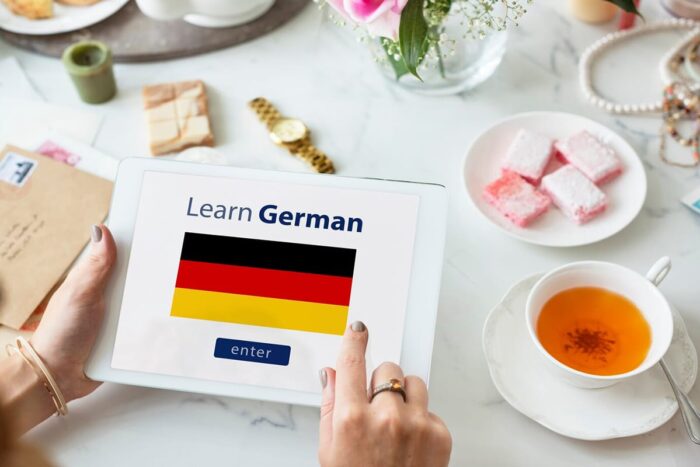 femeie care tine in mana o tableta pe care invata limba germana fundal masa ceai linguatranscript