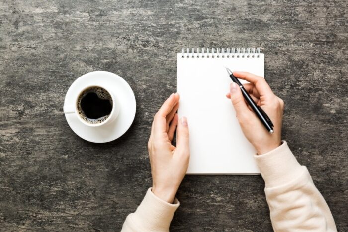 Woman,Hand,With,Pencil,Writing,On,Notebook,And,Hold,Coffee