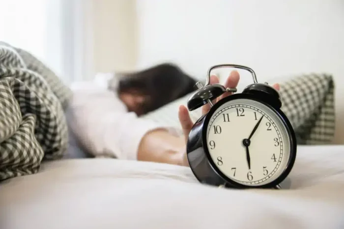 Care sunt cele mai elementare obiceiuri pe care să nu le faci înainte de somn? sleepy woman reaching holding alarm clock 1 scaled 1 1024x684 1.webp