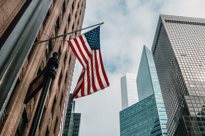 the USA or United States of America flag on a flagpole near skyscrapers under a cloudy sky