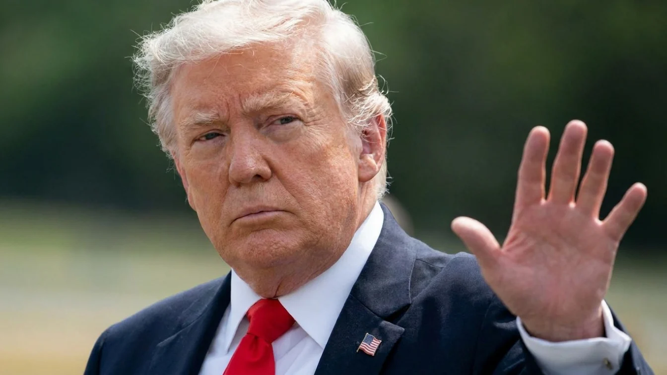 AFP via Getty Images Donald Trump, wearing a suit, raises a hand towards the camera.