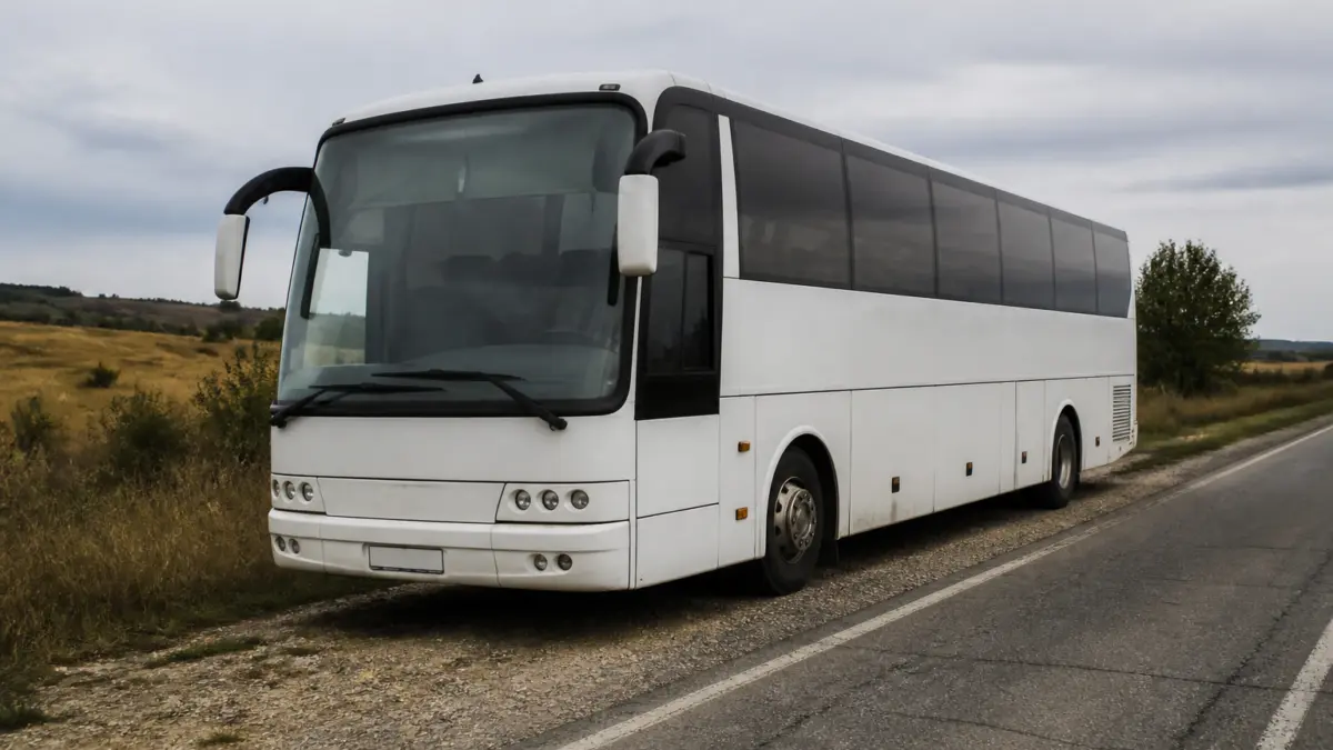 Un autocar alb modern este staționat pe acostamentul pietruit al unui drum asfaltat