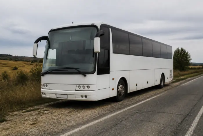 Un autocar alb modern este staționat pe acostamentul pietruit al unui drum asfaltat