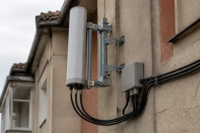 O antenă de telecomunicații albă, cilindrică, montată pe un suport metalic fixat pe peretele exterior al unei clădiri
