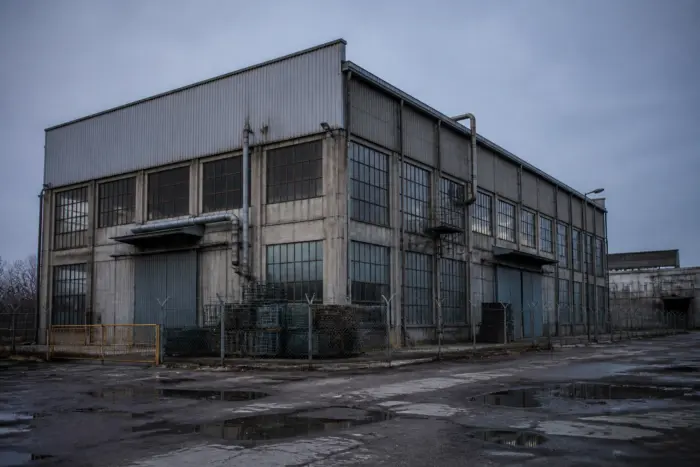 O clădire industrială mare, cu aspect de hală de producție, cu numeroase ferestre pătrate și uși metalice mari la nivelul solului