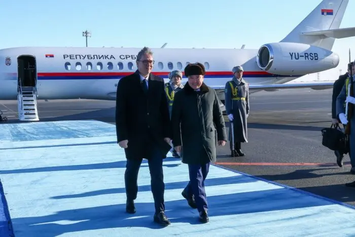 Aleksandar Vucic mergand pe un covor albastru pe pista unui aeroport, langa un alt oficial, in fata unui avion oficial al Republicii Serbia