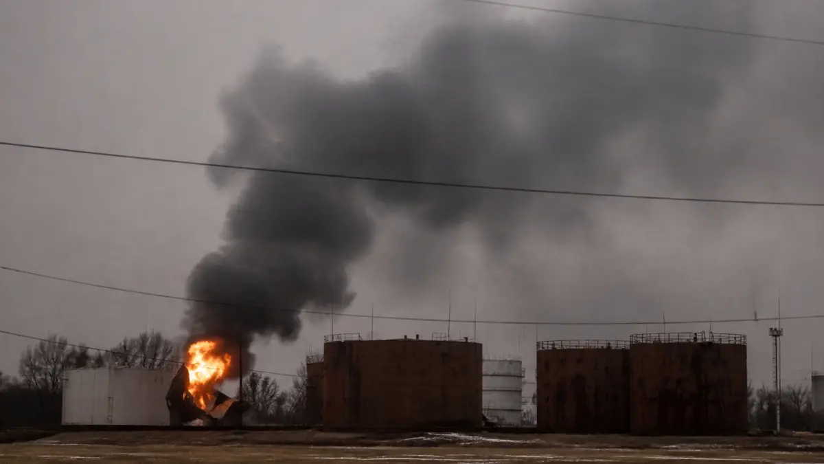 Large black smoke plume and fire rising from an industrial facility with oil storage tanks