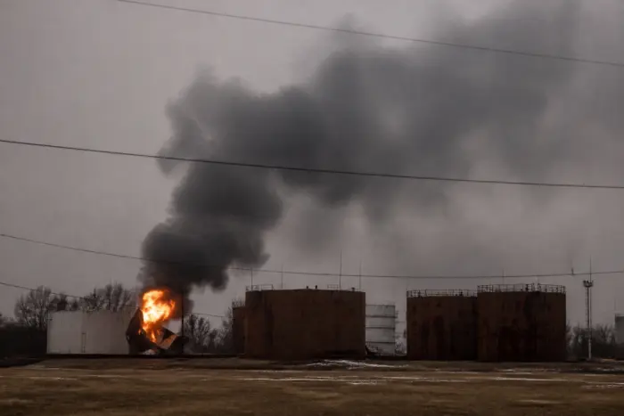 Large black smoke plume and fire rising from an industrial facility with oil storage tanks
