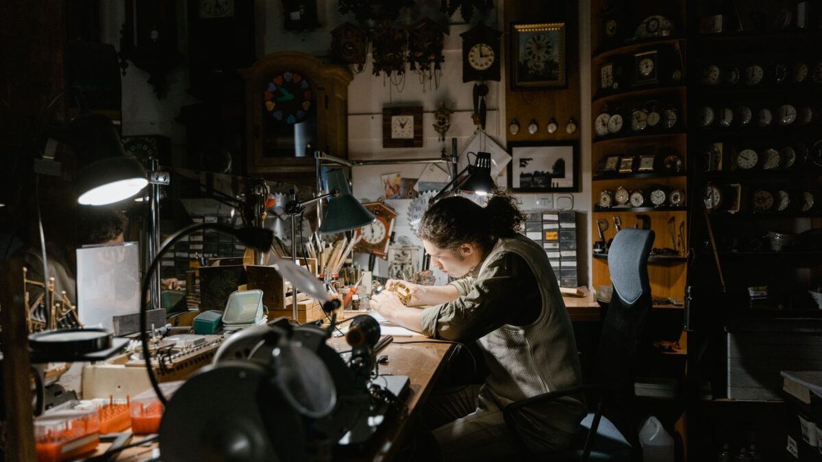 Un ceasornicar lucrează la mecanisme fine într-un atelier plin de ceasuri vechi