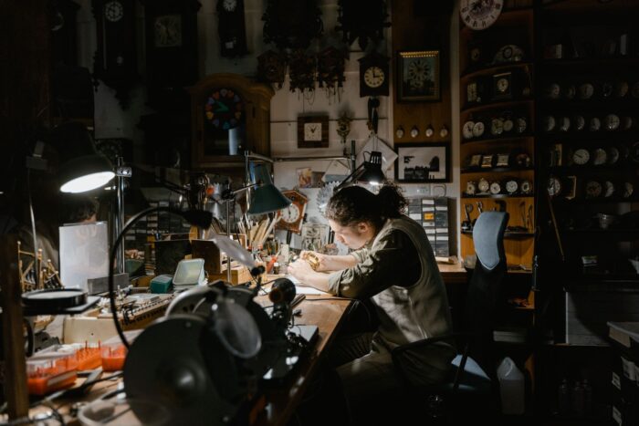 Un ceasornicar lucrează la mecanisme fine într-un atelier plin de ceasuri vechi