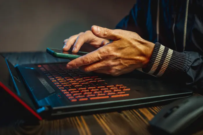 Hands holding a smartphone over a backlit gaming laptop keyboard in a dark setting