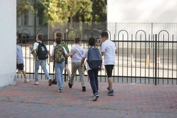 Grup de elevi cu ghiozdane mergând spre incinta școlii