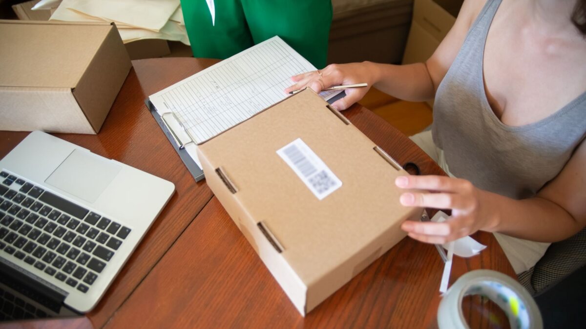 Persoană care pregătește un colet pentru expediere lângă un laptop și formulare