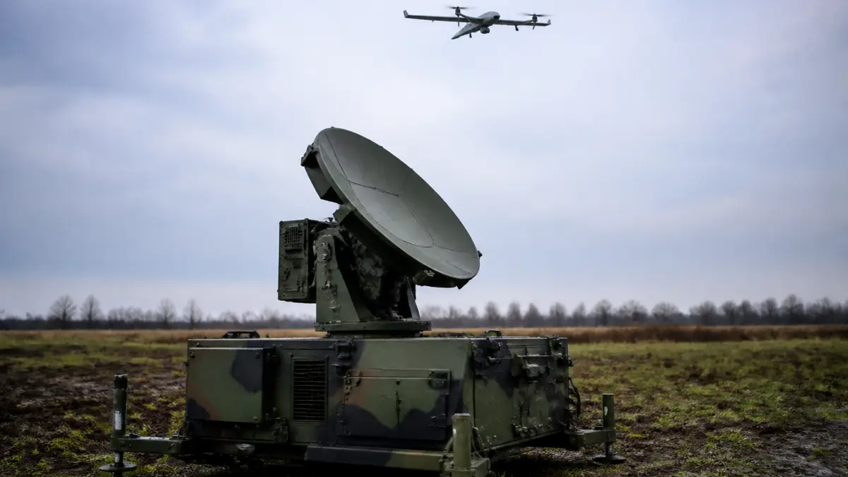 Un sistem de radar militar cu o antenă parabolică mare montat pe o unitate mobilă, aflat într-un câmp deschis sub un cer înnorat