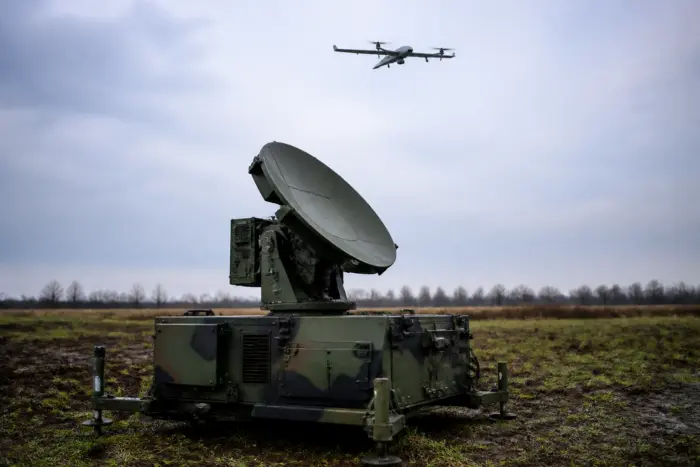 Un sistem de radar militar cu o antenă parabolică mare montat pe o unitate mobilă, aflat într-un câmp deschis sub un cer înnorat