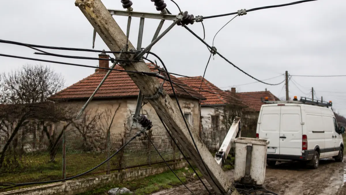O imagine ce surprinde un stâlp de electricitate din beton rupt și înclinat peste un drum noroios de la sat