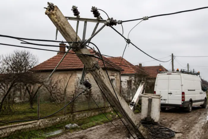 O imagine ce surprinde un stâlp de electricitate din beton rupt și înclinat peste un drum noroios de la sat